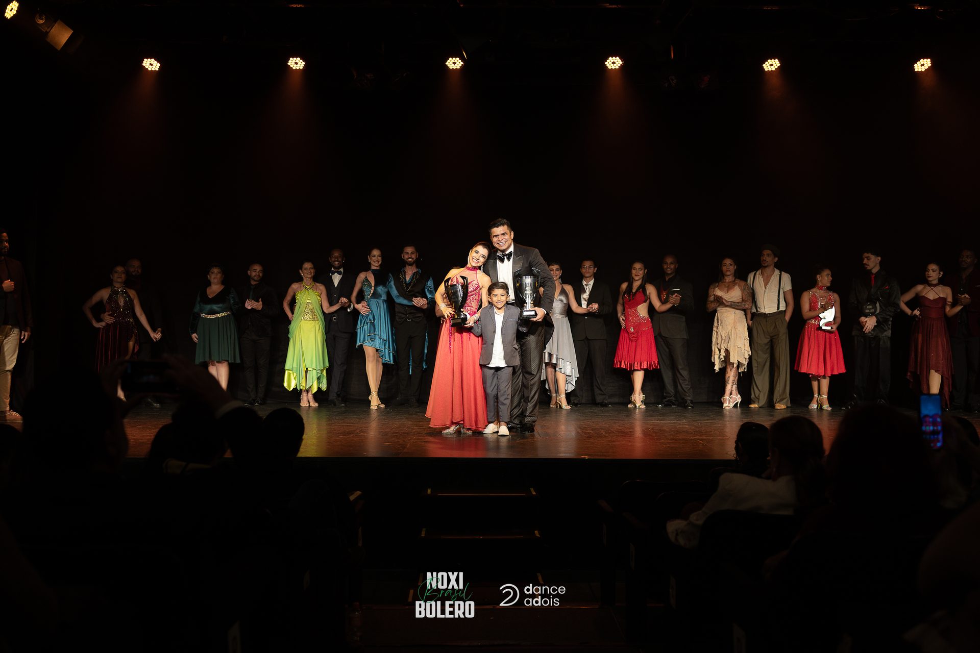Campeões do NOXI Brasil Bolero 2026 com os troféus no palco, ao lado dos competidores da final
